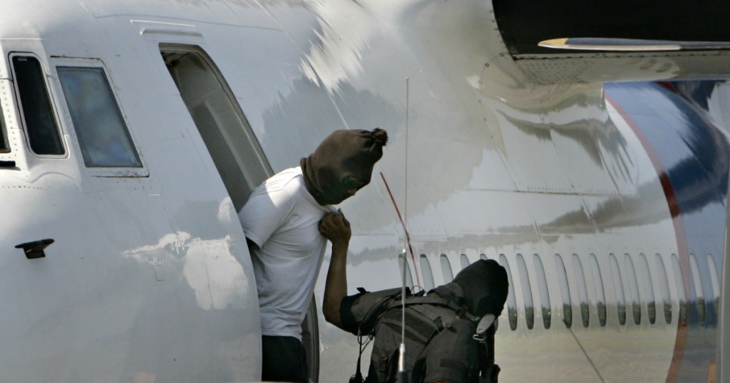 A hooded terror suspect, left, is led off of a plane by a member of Indonesia's elite anti-terror squad, Thursday, July 3, 2008 in Jakarta, Indonesia. Anti-terror police arrested nine suspected Muslim militants and seized a large cache of high-powered bombs, foiling a major attack targeting Westerners in the Indonesian capital, police and media reports said Thursday.(AP Photo/Achmad Ibrahim)